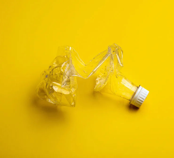 Crushed plastic bottle with white lid on yellow background, symbolizing recycling and sustainable materials used in stonearts® products.