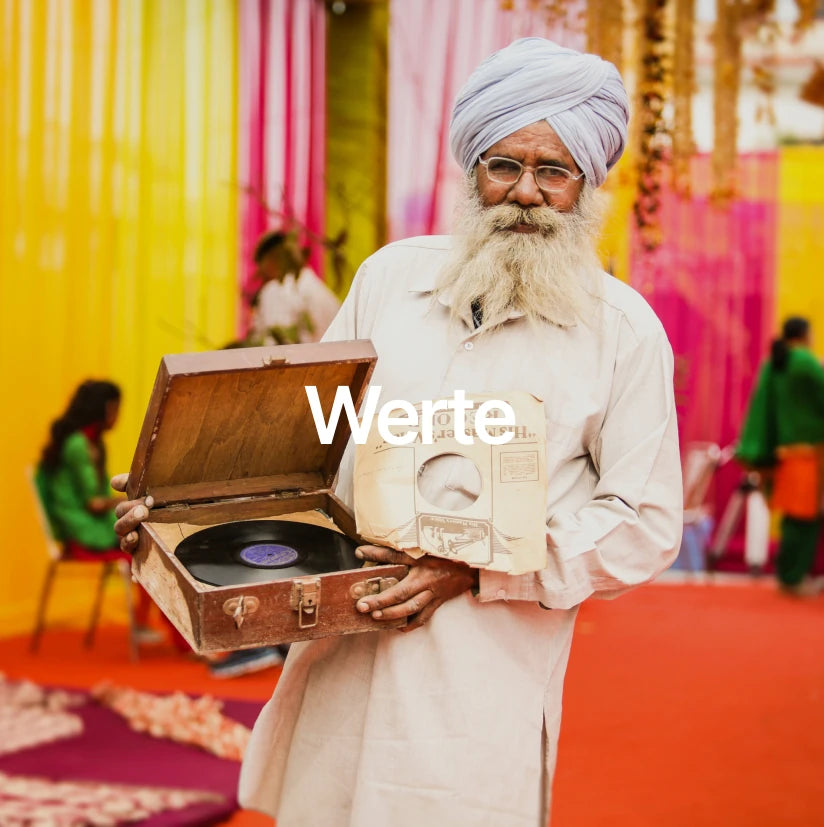 Älterer Mann mit Turban hält einen Plattenspieler, vor einem farbenfrohen Hintergrund, symbolisiert die kulturellen Werte und Traditionen, die stonearts® respektiert und integriert.