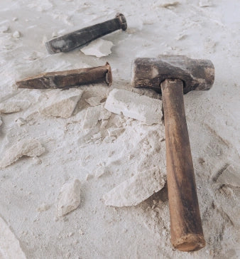 Hammer and chisel lying on light-colored sandstone, surrounded by broken pieces of stone, show the tools for working stonearts® materials.