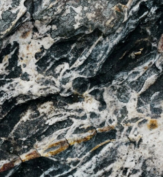 Close-up of the natural surface of a natural stone with a complex texture in shades of gray, white and black.