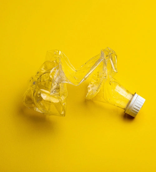 Zerdrückte Plastikflasche mit weißem Deckel auf gelbem Hintergrund, symbolisiert Recycling und Nachhaltigkeit.