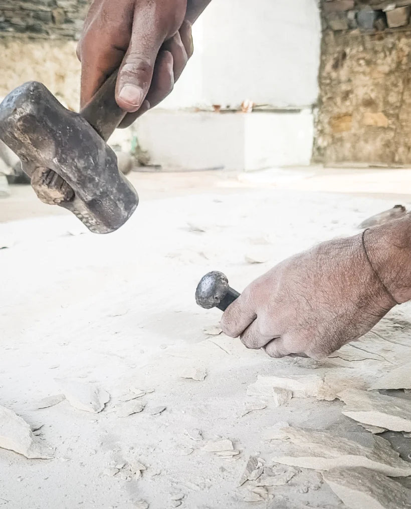 A craftsman works a light-colored stone with a hammer and chisel to create custom stone surfaces for stonearts® acoustic panels and individual wall cladding.