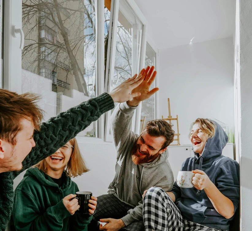 Four people sitting in a bright room, laughing and giving each other a high-five, symbolizing the joy and cooperation in the stonearts® team.