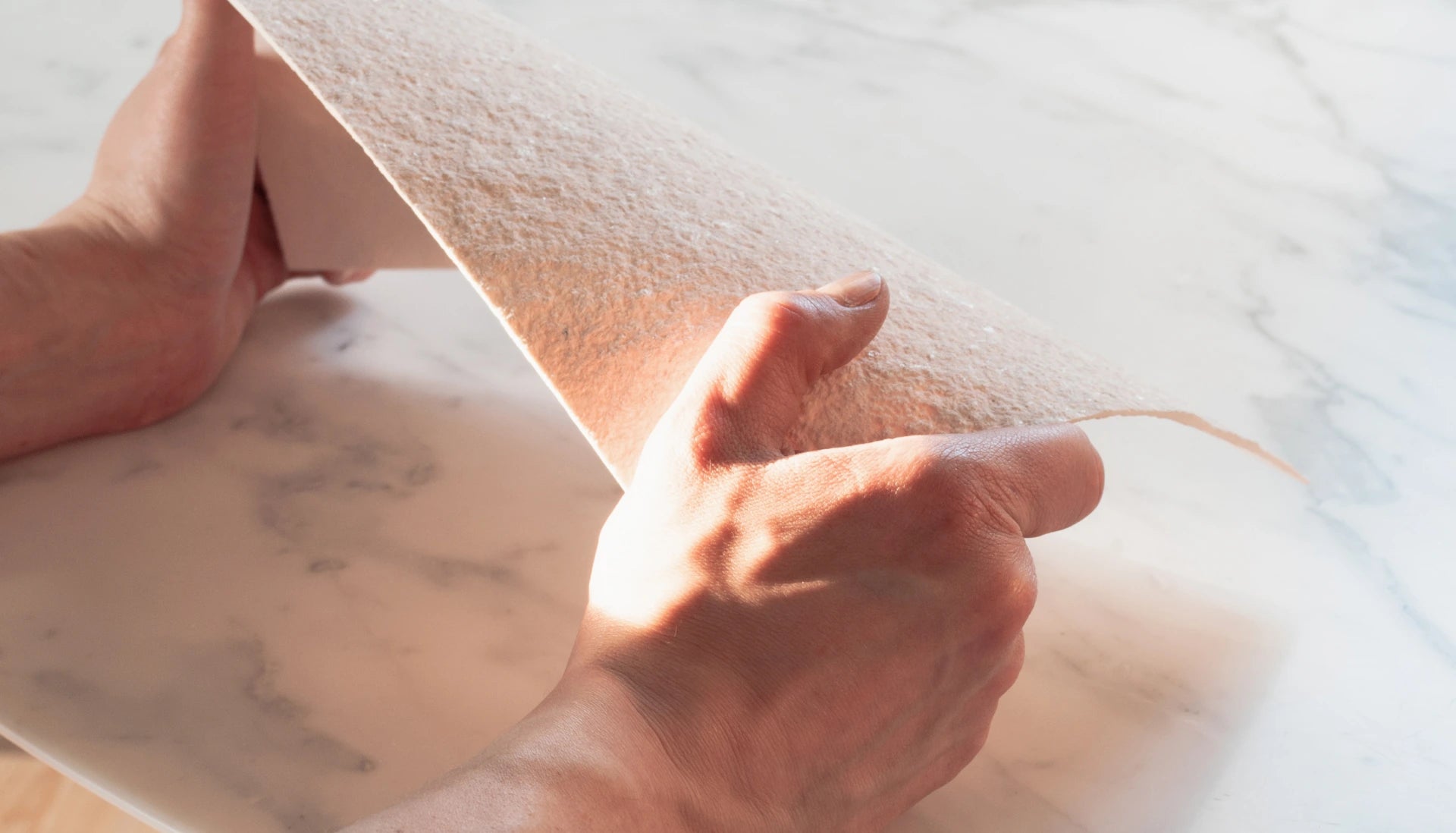 Hands hold a thin, flexible slab of light-colored sandstone used to finish stonearts® acoustic panels and decorative wall cladding, ideal for modern and sustainable interior solutions.